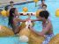 A picture of two children trying to knock each off of their floats in the pool.